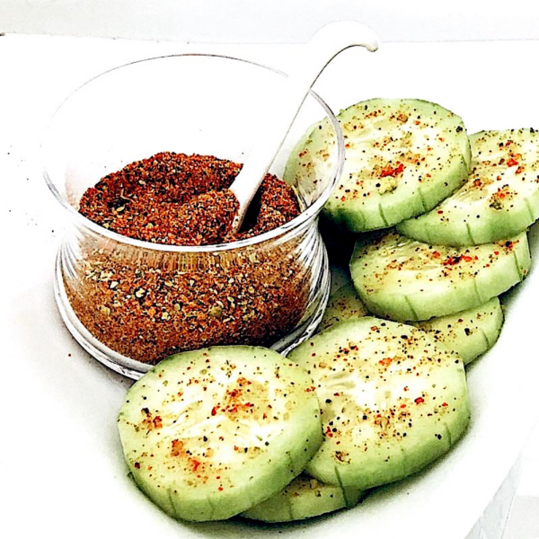 Jar of chile lime salt with a side of sliced cucumbers topped with the chile lime salt.