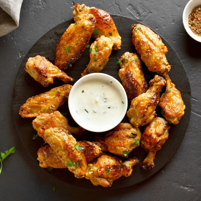 Smoked wings with parmesan rub and a small dish of sour cream dip in the middle of the plate.