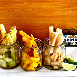 Jars with pineapple, mango and jicama drizzled with chamoy sauce and sprinkled with Tajin (chile lime salt) for example of Mexican fruit cups as street food.