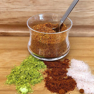 Jar of chile lime salt (Tajin) with lime, chile pepper and salt spread out in front of jar.