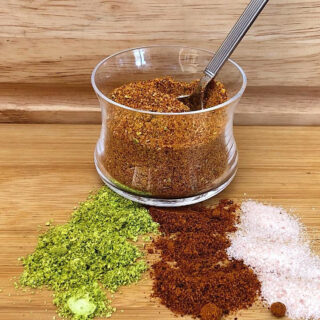 Jar of chile lime salt (Tajin) with lime, chile pepper and salt spread out in front of jar.