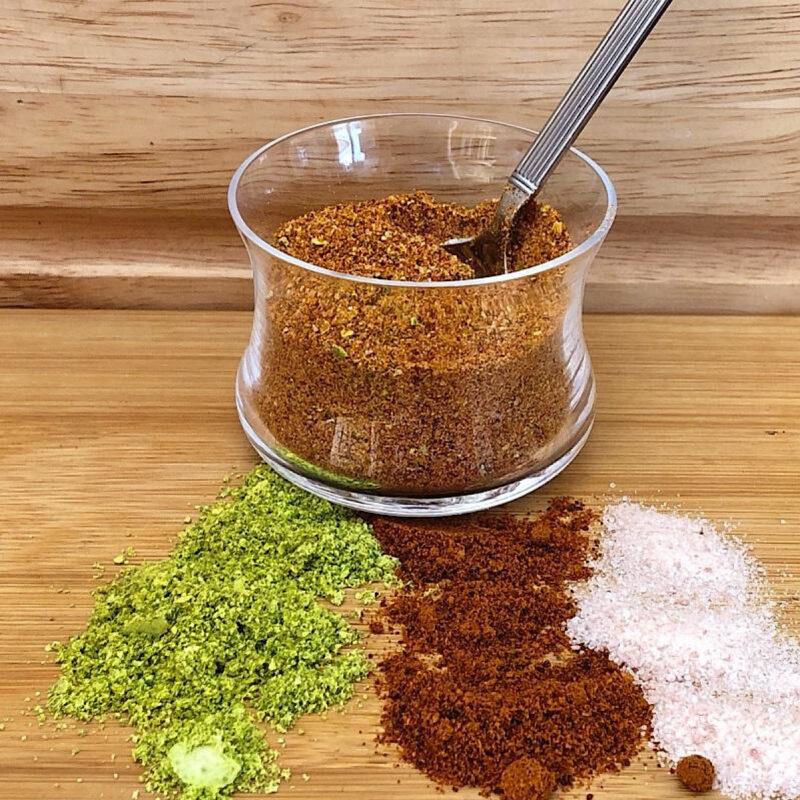 Jar of chile lime salt (Tajin) with dehydrated lime, dried chile pepper and salt spread out in front of jar.
