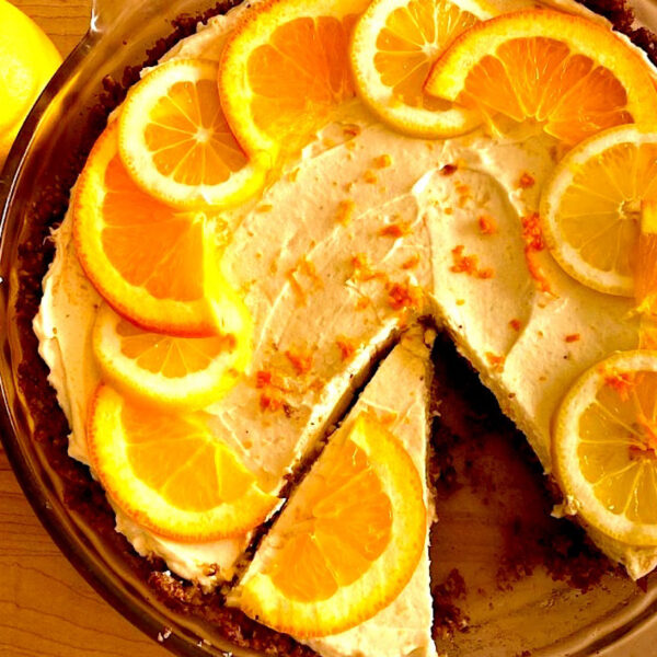Meyer lemon pie in a pie plate with a slice cut out, topped with orange slices.