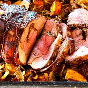 Roasted leg of lamb with Mexican spices, sliced open and surounded by vegetables.