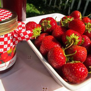 Bowl of fresh strawberries and a jar of strawberry rhubarb jam
