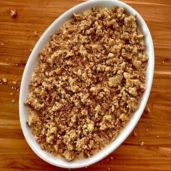 Rhubarb crisp in a white baking dish on a cutting board, ready for the oven.