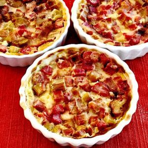 3 white ramekins of rhubarb crisp on a red mat.