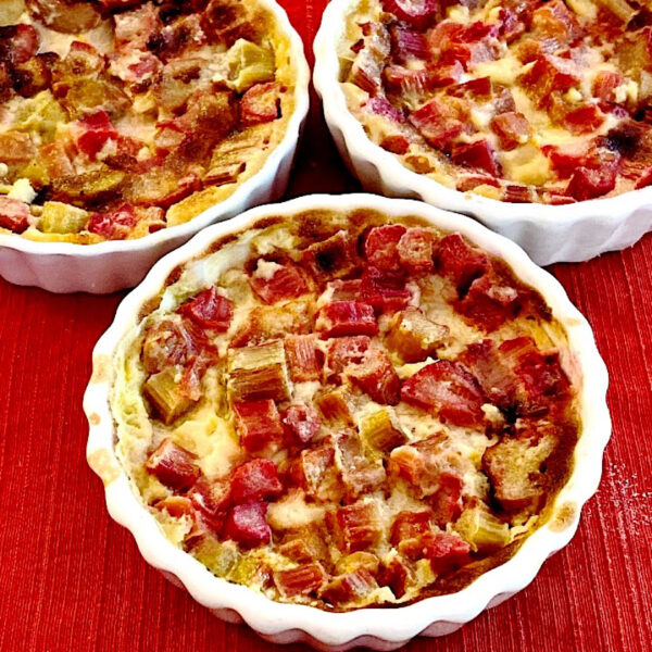 3 white ramekins of rhubarb crisp on a red mat.