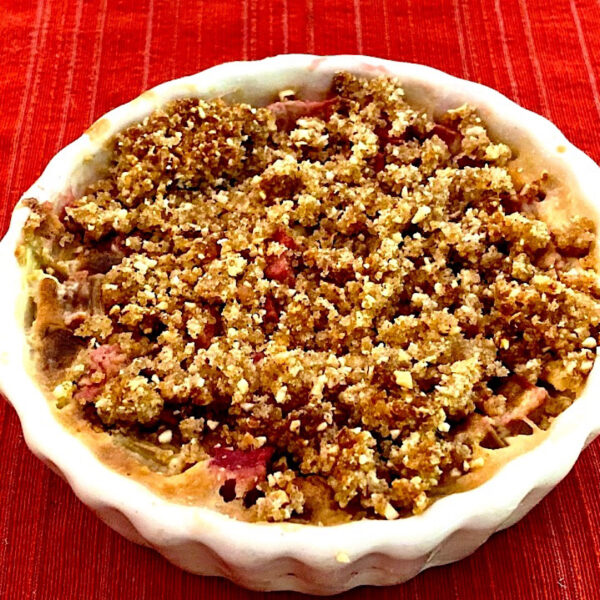 Rhubarb crisp in a white pie plate on a red mat.