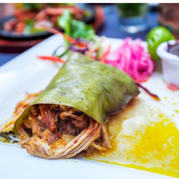 Pulled pork with achiote paste wrapped in a banana leaf on a white plate with pink flowers.