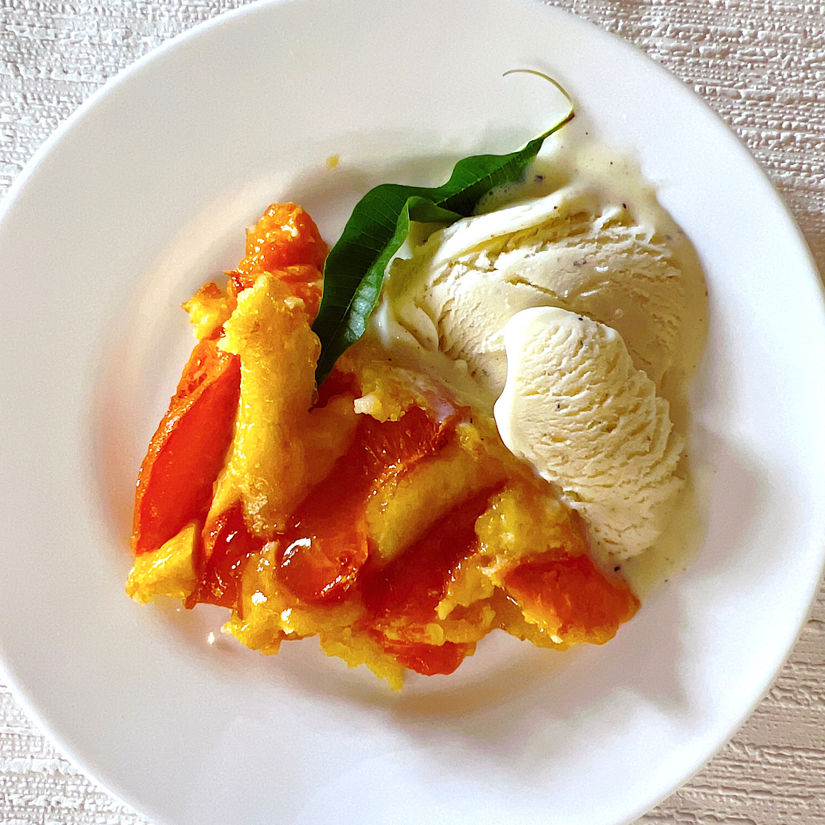 Dish of crustless apricot frangipane with scoop of ice cream and lemon verbena leaf.