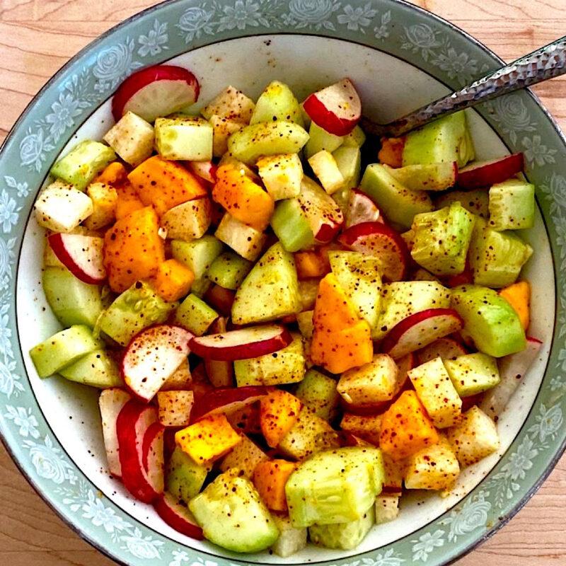Mexican fruit salad with jicama, mango, cucumber, and radish, sprinkled with Tajin (homemade chili lime salt) in a large bowl.
