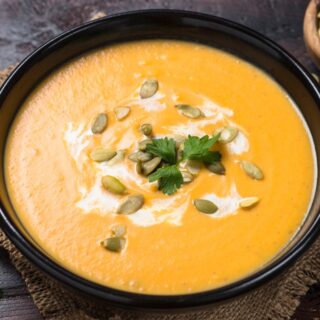 Bowl of pumpkin ancho soup with pumpkin seeds and sour cream garnish.