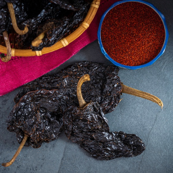 Dried ancho peppers and a small bowl of powdered ancho spice.