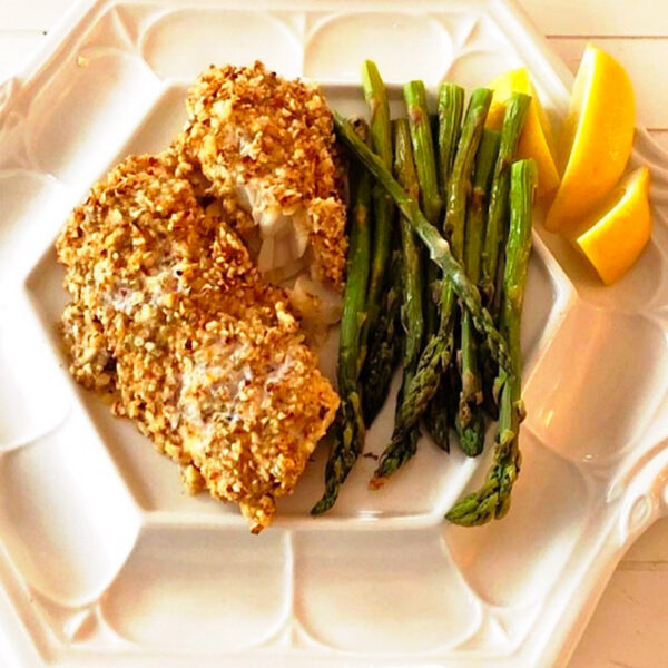 Almond crusted cod with a side of asparagus spears and lemon wedges.