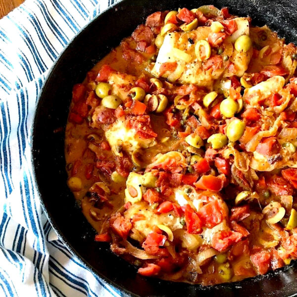 Cod  veracruz  in a cast iron skillet with a blue striped towel