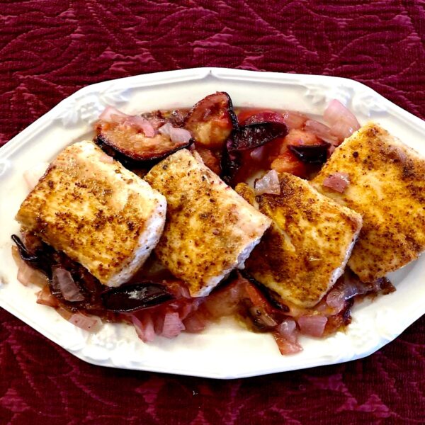 Four mahi mahi filets with a plum sauce On a white plate with a maroon background.