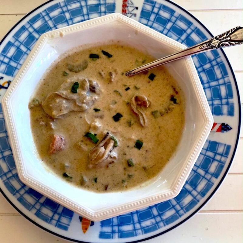 Oyster stew in a white bowl on a patterned blue plate.