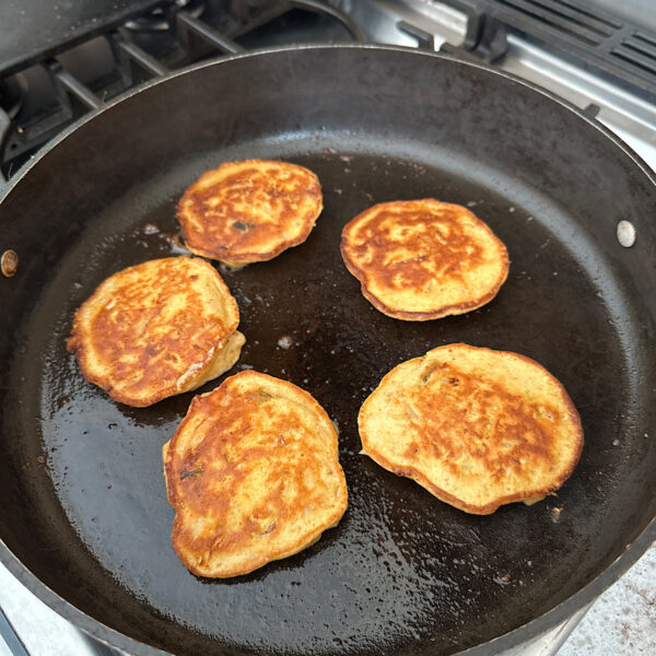 5 kimchi pancakes in skillet after being flipped over, showing golden brown color.