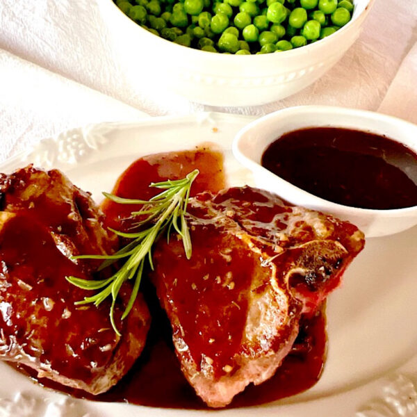 2 lamb chops with cumberland sauce and sprig of rosemary and peas in background.