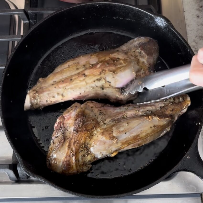 Two lamb shanks being seared in a skillet in prep for osso buco.