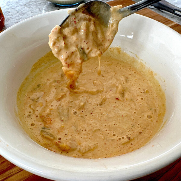 Kodiak pancake batter with kimchi folded in. Spoon held above batter showing thickness.