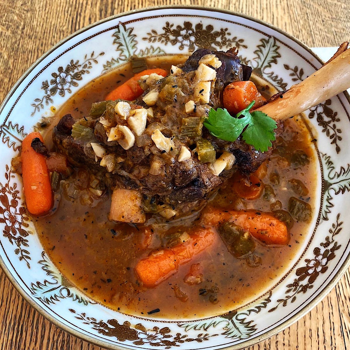 Osso bucco stew in a large bowl with carrots and mushrooms.