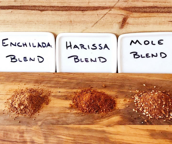 3 spice blends on a wood board; enchilada, harissa and mole spice blends.