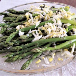 Asparagus spears with crumbled hard boiled eggs on top, on a glass plate.