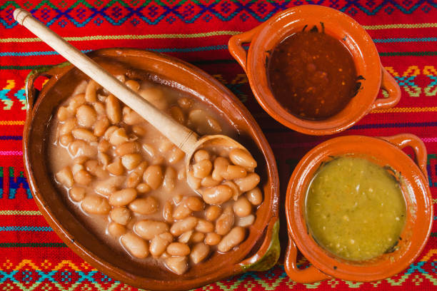 Mexican  bean soup in  clay pot with sides of red sauce and verde sauce.