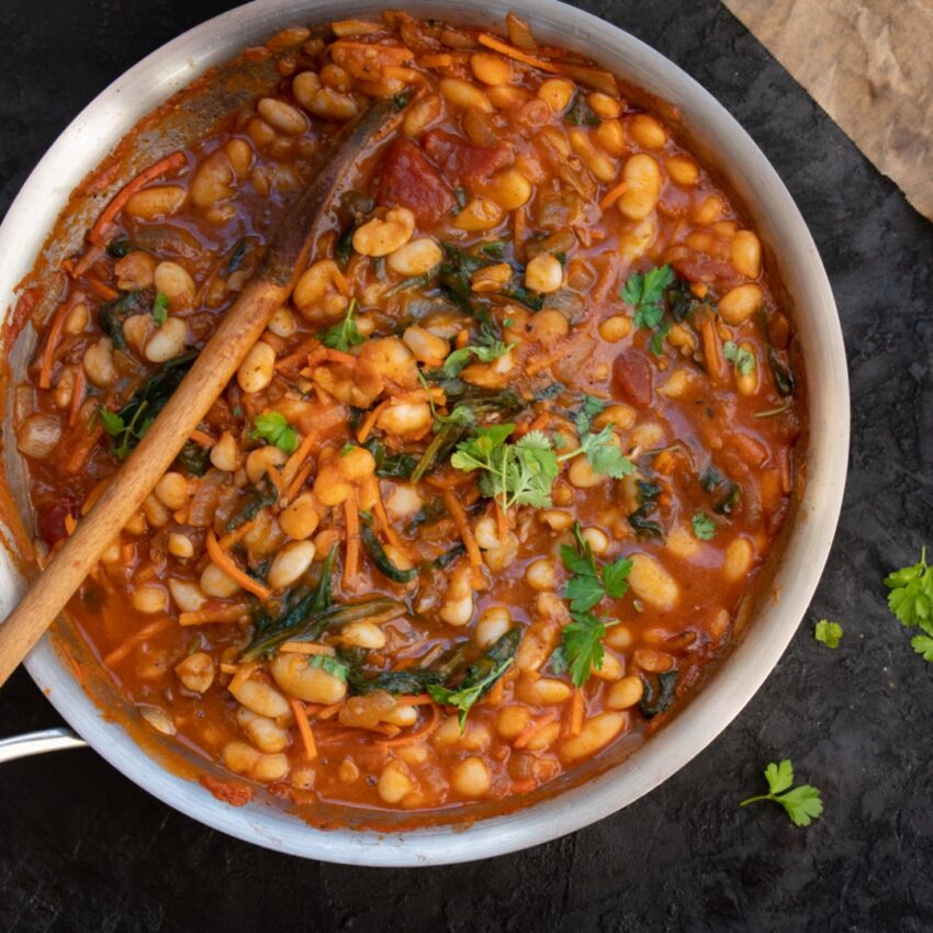 Pot of Tuscan bean stew with white beans, cabbage and sausage and garnished with parsley.
