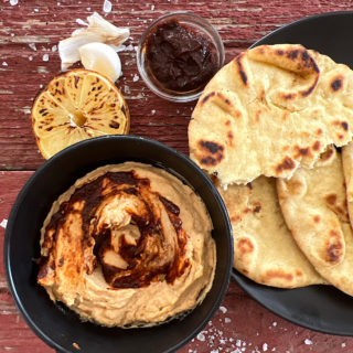 Bowl of harissa hummus with side of toasted pita bread.