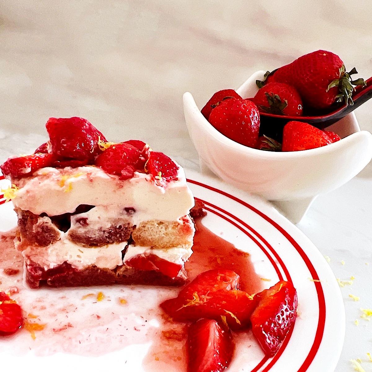 Slice of strawberry tiramisu on a plate with a bowl of strawberries behind it.