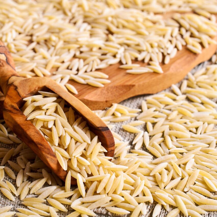 Orzo pasta on a wooden plate and inside a wooden scoop.