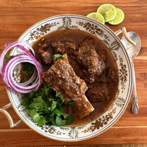 Large dish of beef birria stew with short ribs and garnished with red onions and parsley.