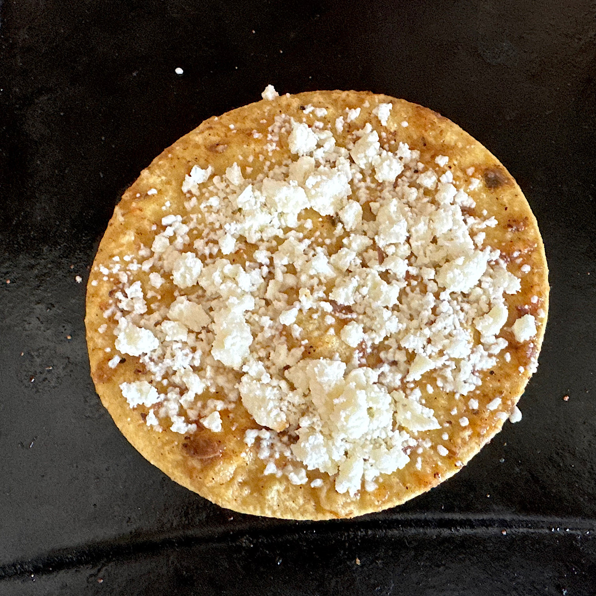 Tortilla on a griddle sprinkled with queso Mexican cheese.