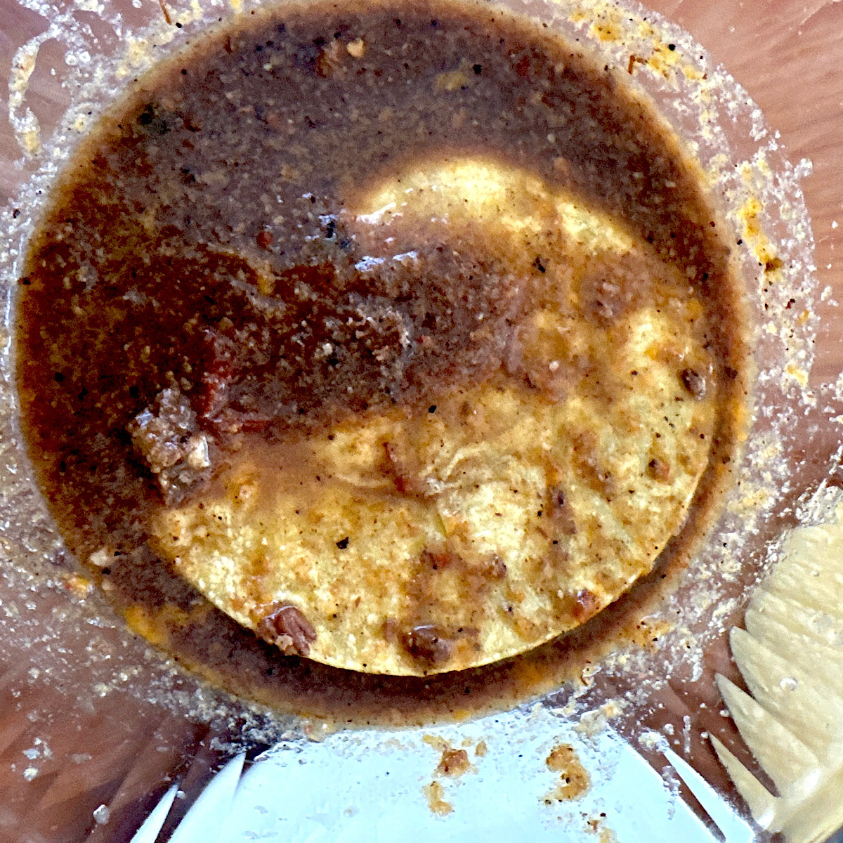 Corn tortilla being dipped in birria beef consomme in a glass bowl.