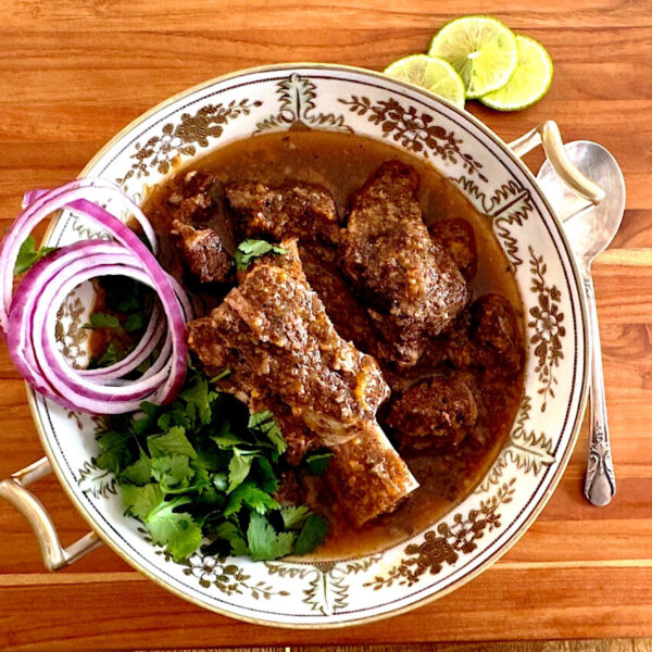 Large dish of beef birria stew with short ribs and garnished with red onions and parsley.