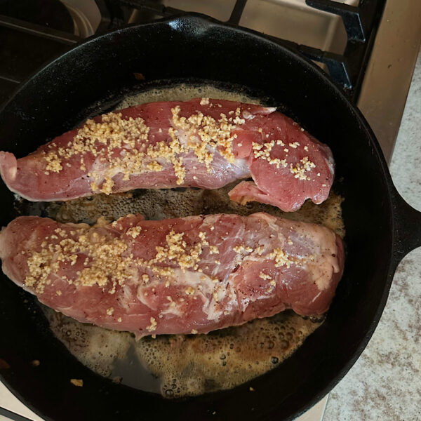 2 pork tenderloins cooking in a cast iron skillet