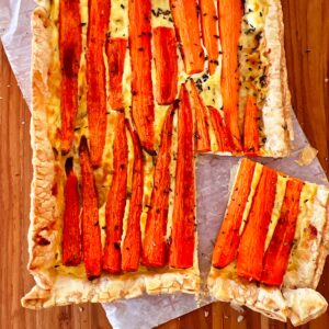 Spring carrot tart on piece of parchment paper, with one square cut and angled.
