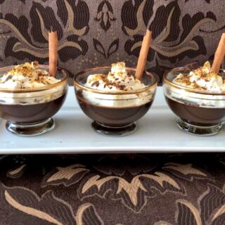Low carb chocolate pots with whipped cream and cinnamon stick garnish.