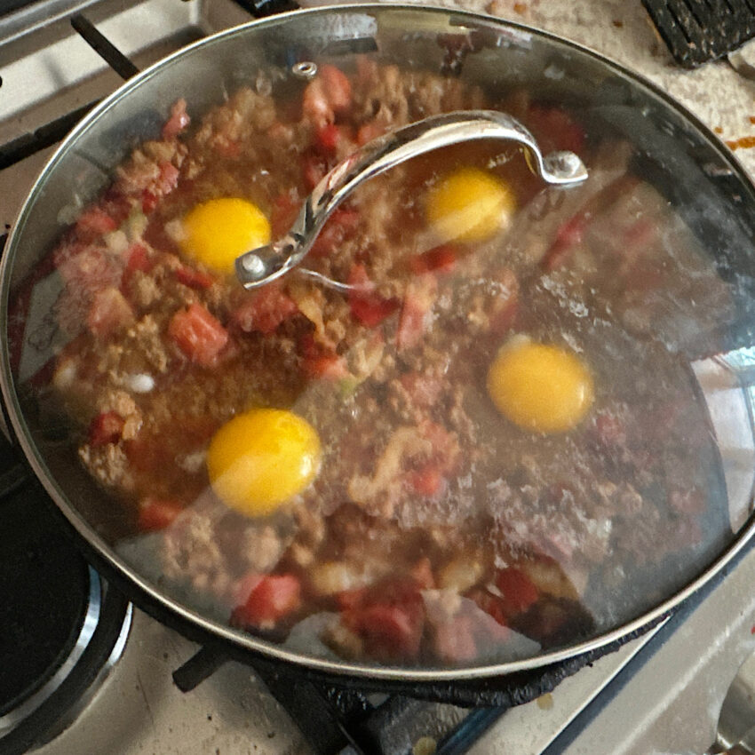 Chorizo mix and eggs cooking with a cover, which is baking the eggs.