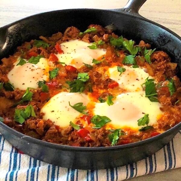 Cast iron skillet low carb dinner of chorizo and eggs with scallions as garnish.