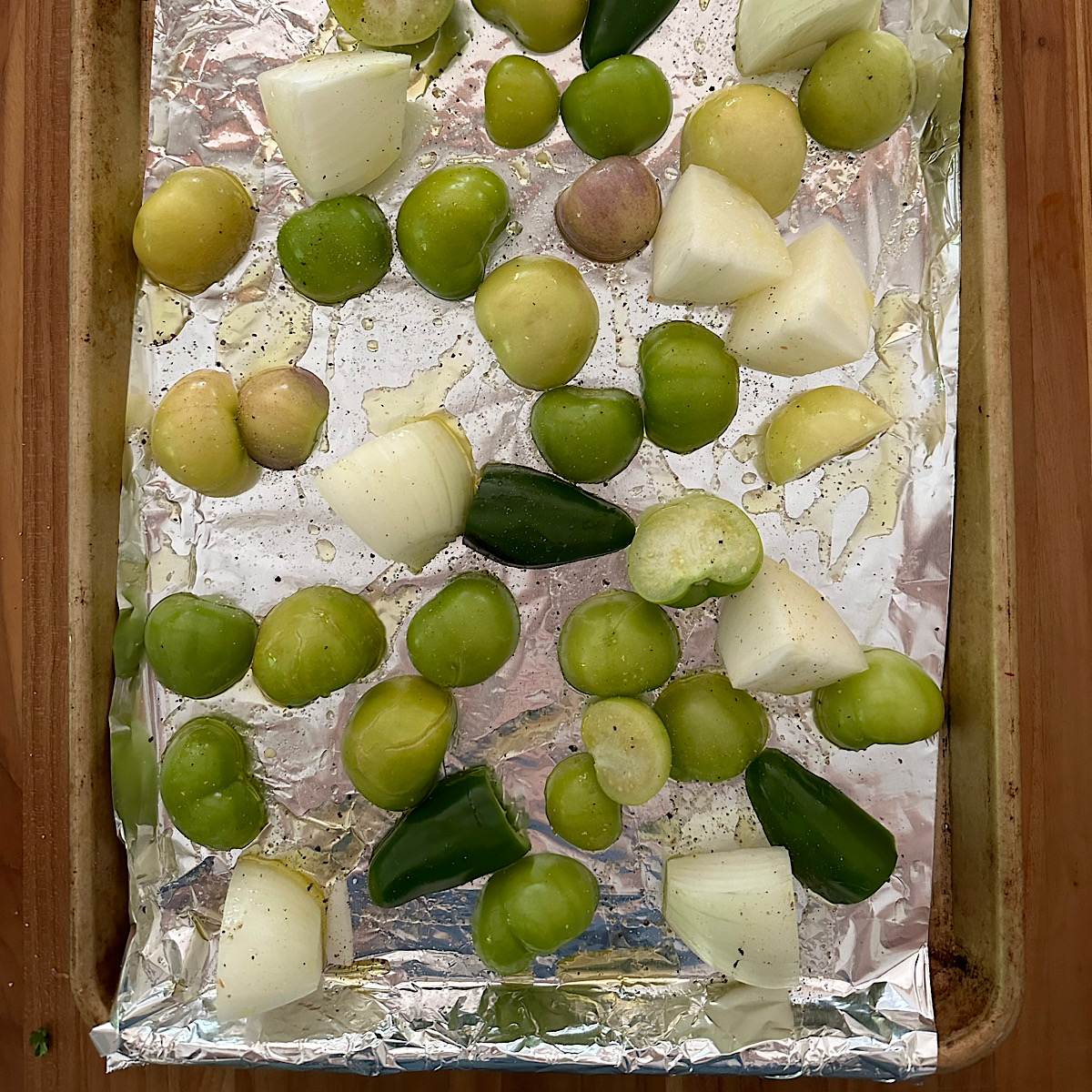 Tomatillos, jalapenos and onions on a baking sheet lined with foil.