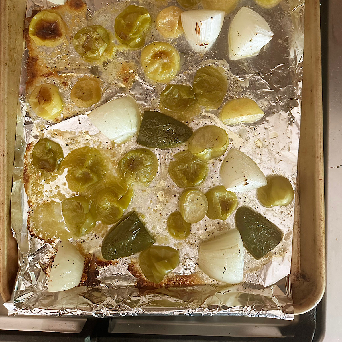 Roasted tomatillos and jalapenos on foil lined baking sheet