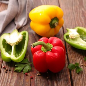 Red, green and yellow bell peppers on a wood cutting board.