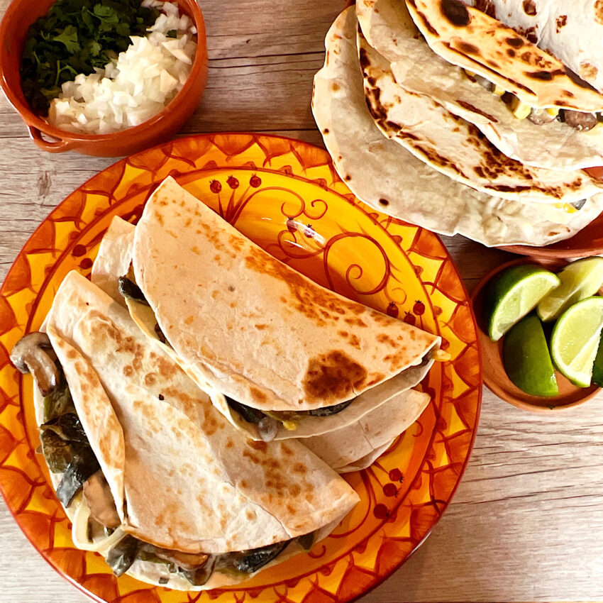 Quesadillas Rajas con Crema on a plate with garnishes on the side.