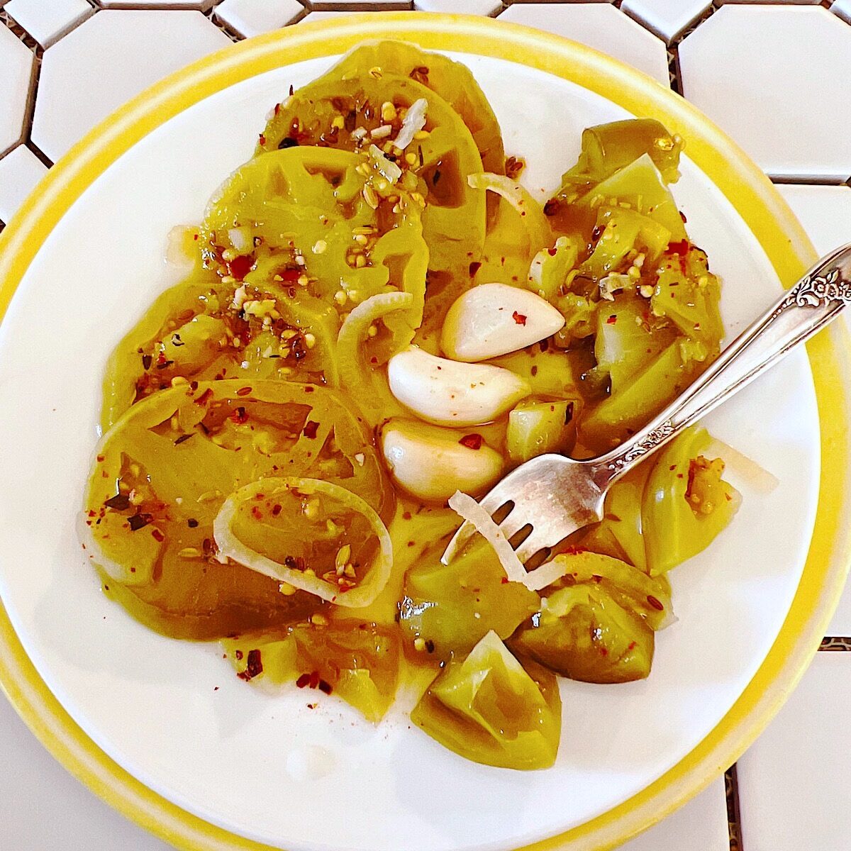 Plate of green tomato pickles with 3 garlic cloves.