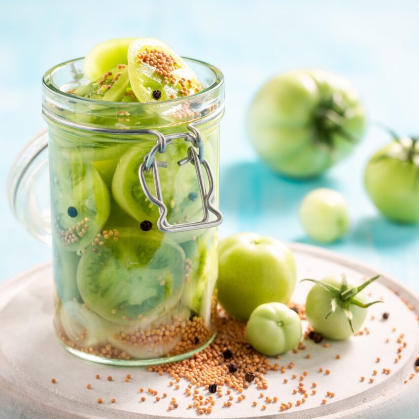 Sliced green tomatoes with pickling spices in a glass jar.