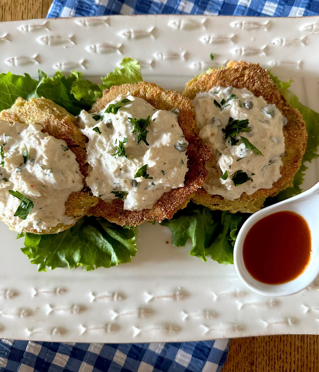 3 fried green tomatoes  with crab salad topping on a bed of lettuce and a side of hot sauce.